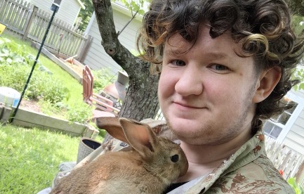 A man in a button-down shirt cradles a young rabbit against his chest.