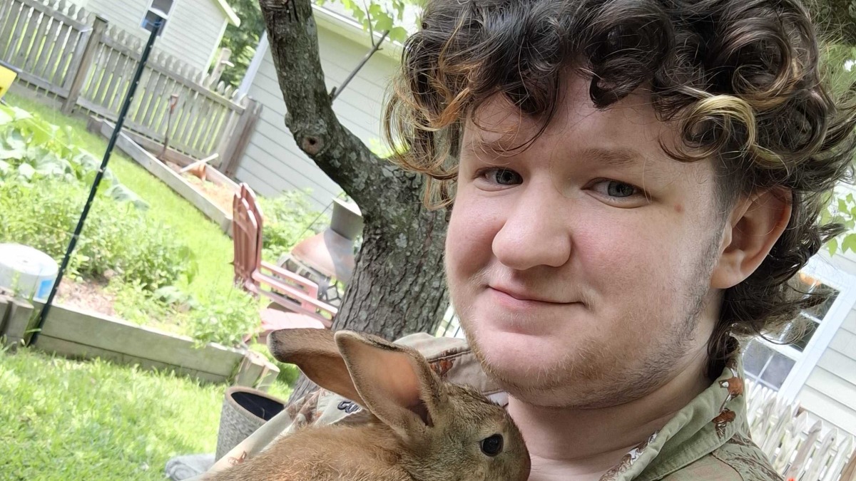 A man in a button-down shirt cradles a young rabbit against his chest.