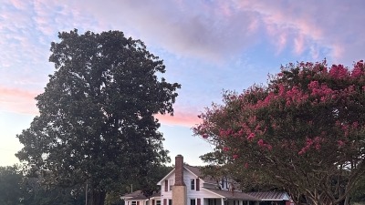 White farmhouse with red trim in front a colorful evening sky