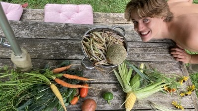 Photo of Conlan Lamb with a smile, sweet corn, tomatoes, Tendersweet carrots, Ridgeway cantaloupe, and Black Turtle dry beans grow in 2024 garden. 