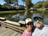 Lily and Dany smiling in a selfie by a lake, both wearing caps and sunglasses