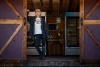 Myself, a smiling woman in dirty jeans and a flannel, leaning against the open door of the shed-turned-farmstand. Fridges and shelves are stocked with produce and cut flowers behind me. 