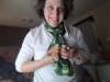 Woman in white shirt and green scarf with short, brown, curly hair holding 3 young chicks